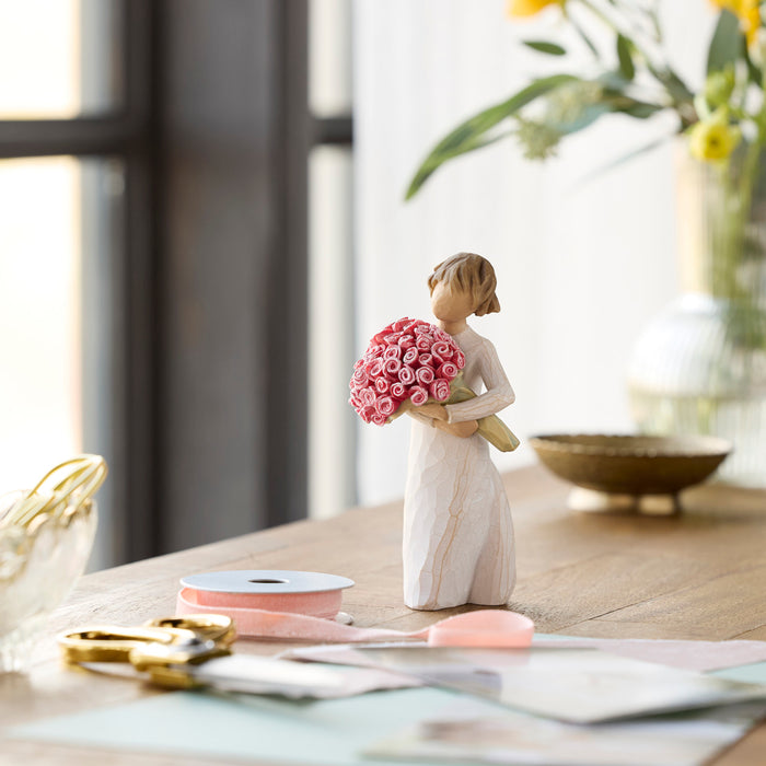 Standing figure in cream dress holding large bouquet of pink roses