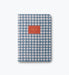 A two-tone blue and white gingham patterned notebook with a terracotta orange label on the front, photographed on a clean white background.