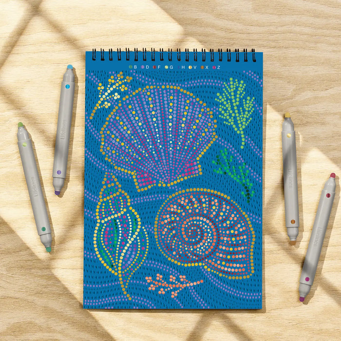 Notebook with colorful shell design on a wooden surface with pens.