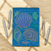Notebook with colorful shell design on a wooden surface with pens.