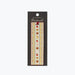 A decorative bookmark from Rifle Paper Co. in its original black hanging card packaging, featuring a vertical strip with a cream background and a whimsical pattern of red apples, brown baskets, and small yellow flowers.