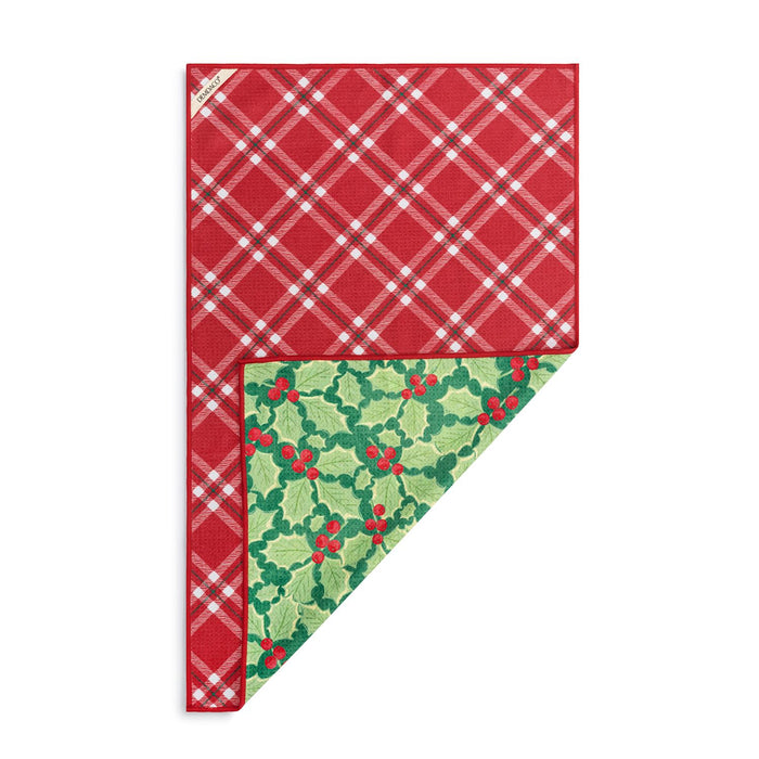 A folded holiday-themed table linen or napkin set on a white background, featuring a red and white plaid pattern on the top section and a green holly and berry pattern on the bottom folded corner.