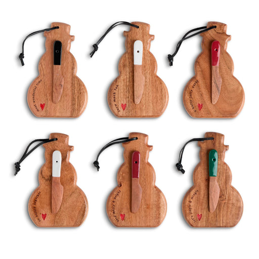 Six wooden Christmas ornament shapes arranged in two rows on a white background, each with a small knife hanging from a black cord and engraved with holiday phrases and a small red heart.