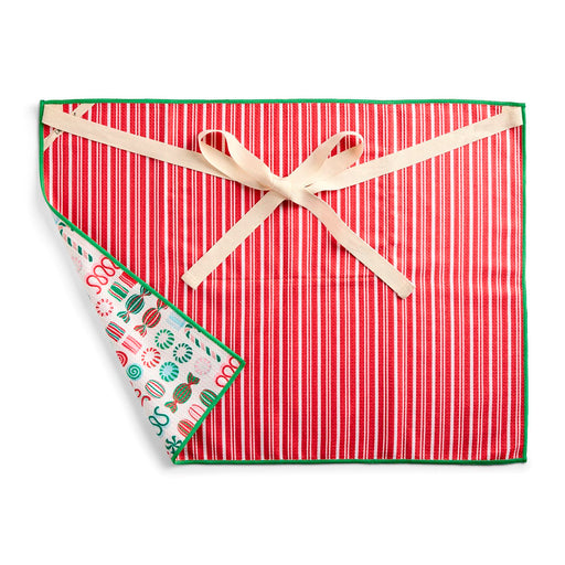 A square red holiday-themed cloth napkin with vertical red and white stripes, a green border, a cream ribbon tied in a bow, and a folded corner showing a white reverse side with colorful candy illustrations.