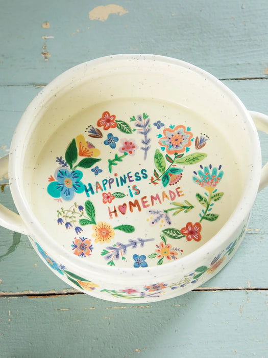Decorative pot with floral design and 'Happiness is Homemade' text on a blue wooden surface