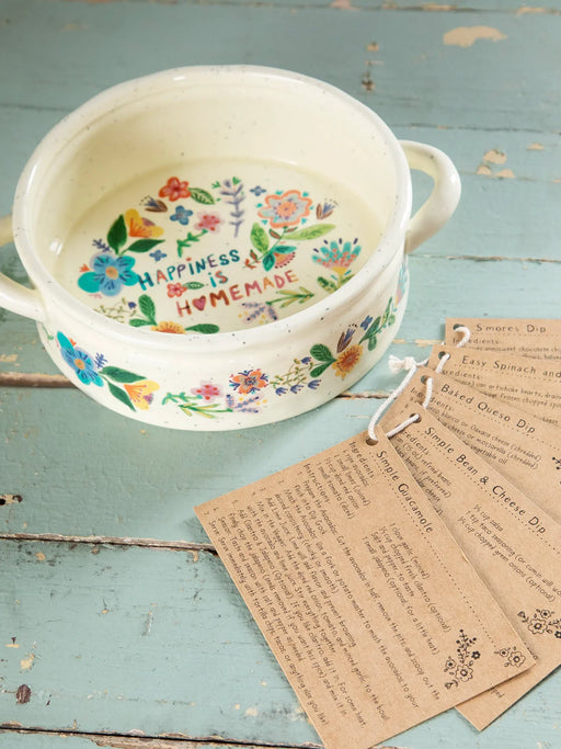 Decorative ceramic bowl with floral design and text on a rustic wooden surface with recipe cards.