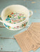 Decorative ceramic bowl with floral design and text on a rustic wooden surface with recipe cards.