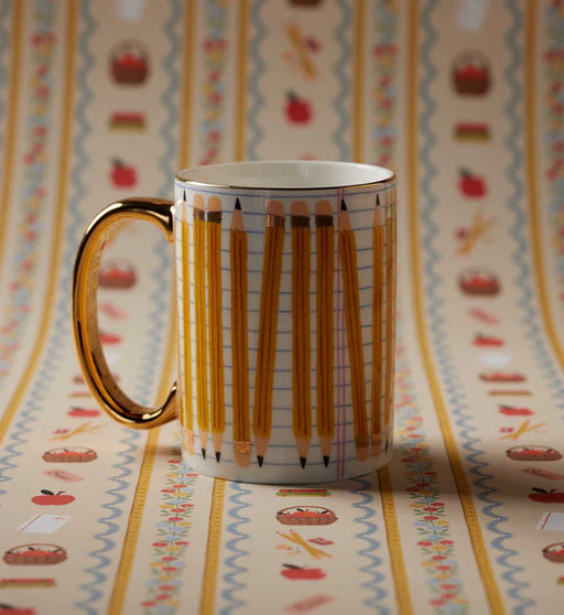 A white ceramic mug with a gold handle and gold rim, decorated with a pattern of yellow pencils on graph paper, set against a matching patterned background.