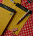 A styled flat-lay of yellow lined notepad pages with black headers reading 'Notepad' and decorative doodles, accompanied by a white pen with gold trim, paper clips, and a small pink eraser on a red-and-white gingham surface.
