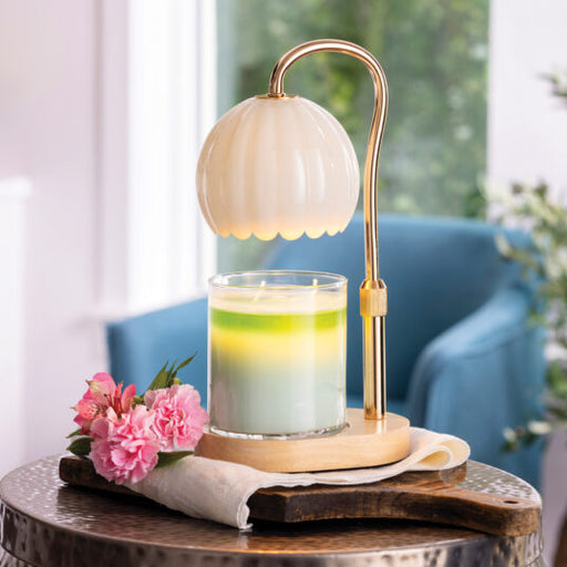 Decorative lamp with a glass candle holder on a wooden table, surrounded by pink flowers and a blurred indoor background.
