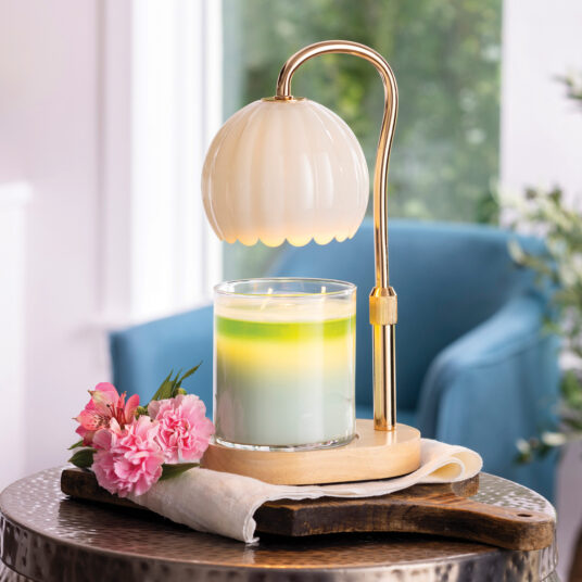 Decorative lamp with a glass candle holder on a wooden table, surrounded by pink flowers and a blurred indoor background.