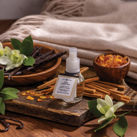 Vanilla extract bottle with vanilla beans, cinnamon sticks, and flowers on a wooden surface.