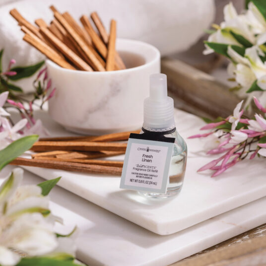 Small bottle of fresh linen spray on a marble surface with cinnamon sticks and flowers.