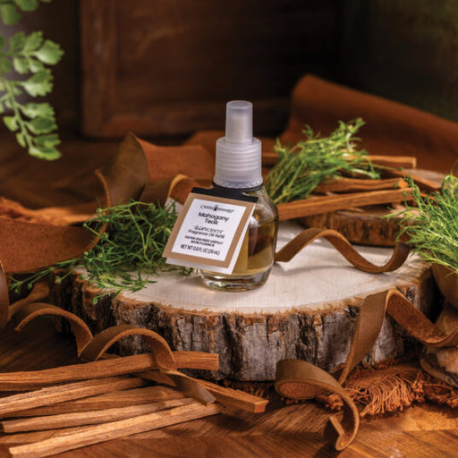 Small bottle of essential oil spray on a wooden stump with cinnamon sticks and greenery.