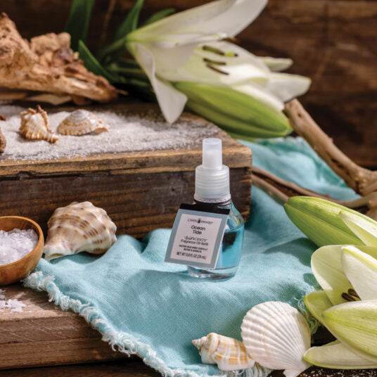 Small bottle with a label on a turquoise cloth surrounded by seashells and lilies