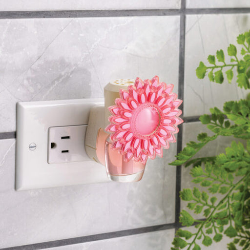 Pink flower-shaped night light attached to a wall socket with a plant in the background.