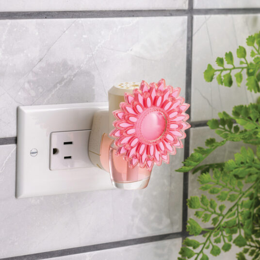 Pink flower-shaped night light attached to a wall socket with a plant in the background.