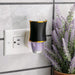 Black and gold night light attached to a wall socket with a potted plant in the background.