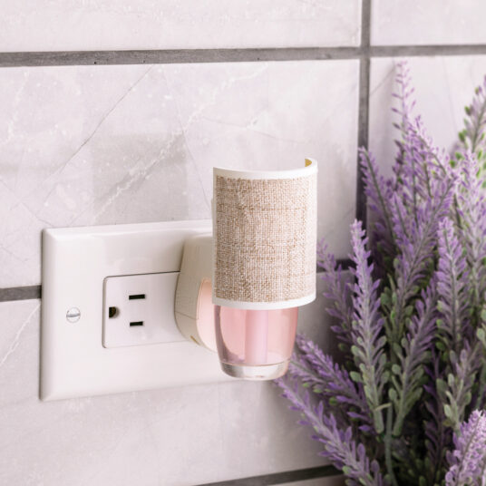 Wall-mounted night light with a beige fabric shade next to a lavender plant on a tiled wall.