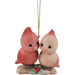 A Christmas ornament featuring two cute, stylized birds perched on a small branch with red berries. One bird is coral pink and the other is pale peach, both with large black eyes.