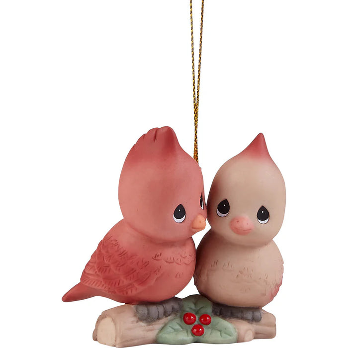 A ceramic Christmas ornament depicting two kissing birds, one pinkish-red and one pale peach, sitting on a small branch with red berries, complete with a gold hanging string.