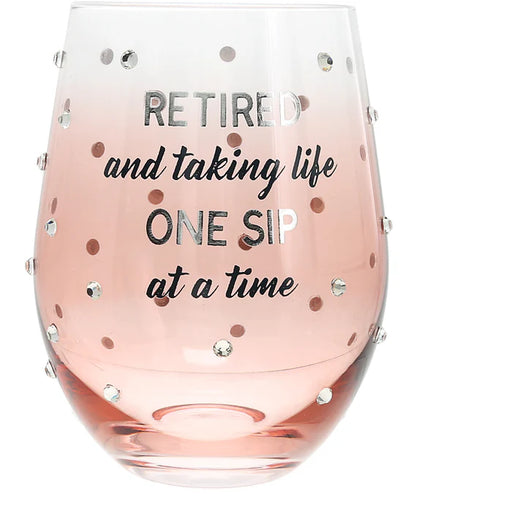 Pink wine glass with text 'Retired and taking life one sip at a time' and decorative studs on a white background