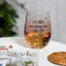 Stemless wine glass with 'Retired and taking life one sip at a time' text, filled with amber liquid, on a magazine with a blurred background.