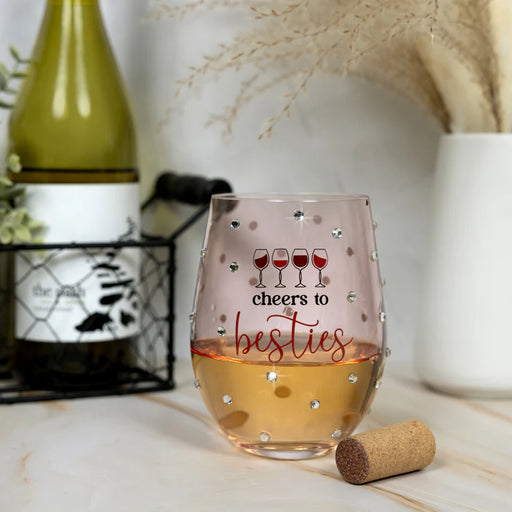 Stemless wine glass with 'cheers to besties' text and wine bottle in the background