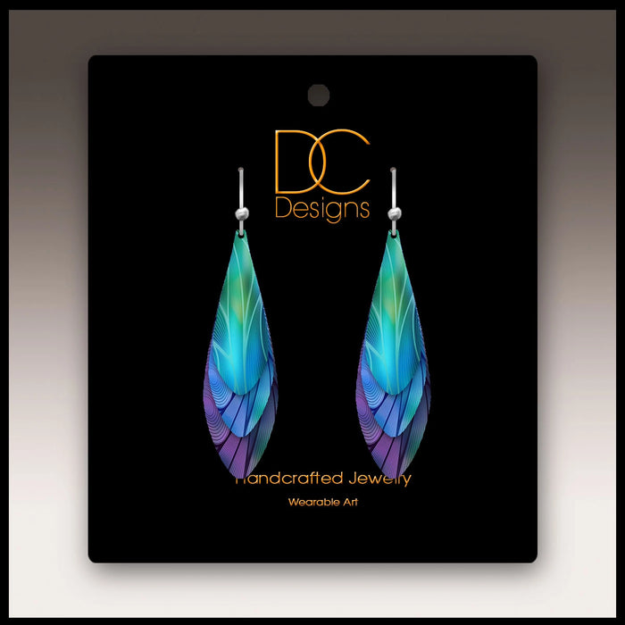 Colorful feather-shaped earrings on a black card with 'DC Designs' branding.
