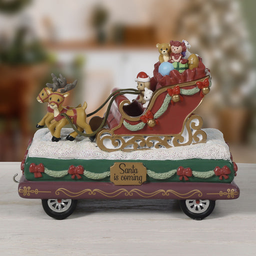 Decorative Christmas scene with Santa's sleigh, reindeer, and toys on a wooden surface.