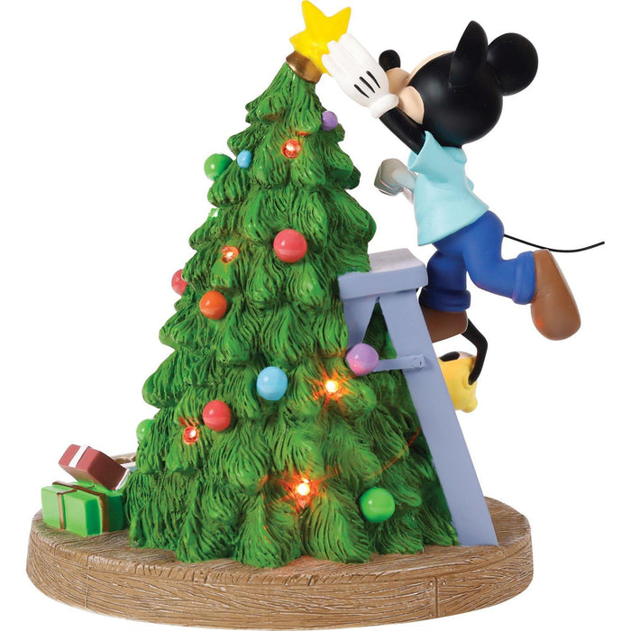Mickey Mouse decorating a Christmas tree with lights and ornaments on a white background