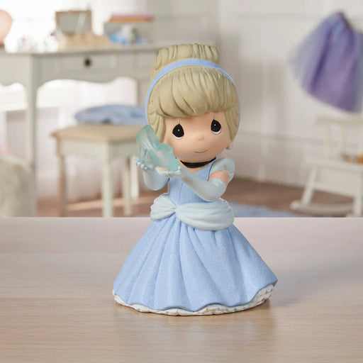 Figurine of a girl in a blue dress holding a glass slipper on a wooden surface.