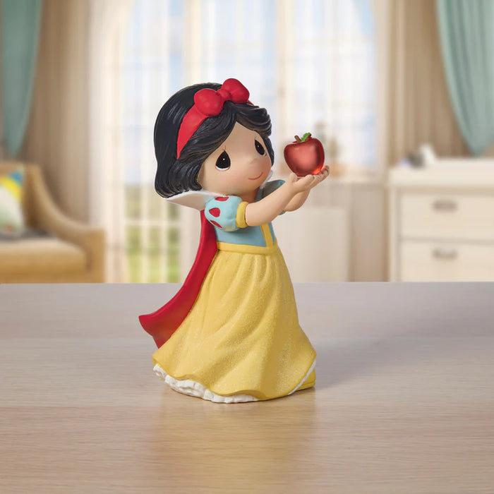 Figurine of a princess holding an apple on a wooden surface with a blurred background