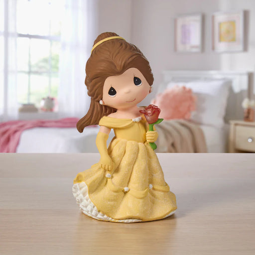 Figurine of a princess in a yellow dress holding a rose on a table with a blurred bedroom background.
