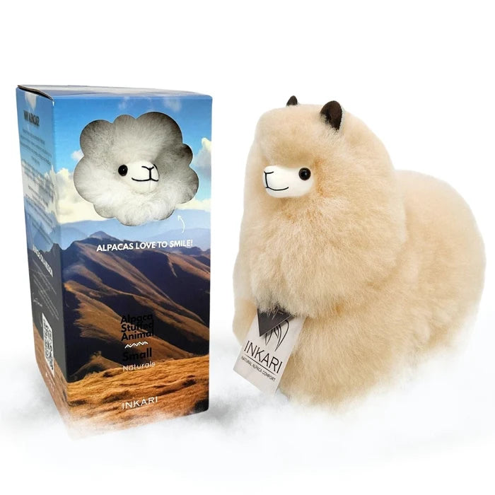 A fluffy cream-colored alpaca plush toy standing next to its retail box on a white background. The box features a blue mountain landscape design with a cloud-shaped cutout showing the smiling alpaca face.