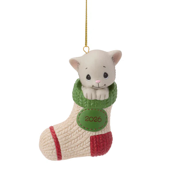 A Christmas ornament shaped like a white kitten peeking out of a knitted stocking. The stocking is cream-colored with red and green knit details, and a green patch on the front that reads '2026'.