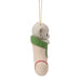 A Christmas ornament shaped like a baby bear peeking out of a knitted cream stocking with a green cuff, hanging from a gold string against a white background.