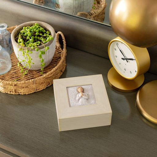 Cream-colored square wood box with hinged lid: Carving of figure in cream dress, with hands in prayer position, surrounded by leaves and vines on lid of box
