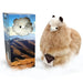 A fluffy alpaca plush toy next to its retail box. The plush is cream and tan with black ears and a small white patch on its face.