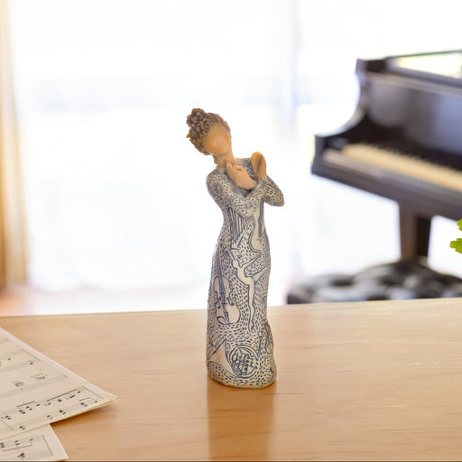 Figure wearing garment carved and painted with contrasting pattern of musical symbols, instruments, and dancing forms. Figure has lighter skin and hair color
