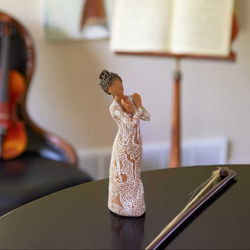 Figure wearing garment carved and painted with contrasting pattern of musical symbols, instruments, and dancing forms. Figure has darker skin and hair color
