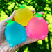 Four colorful stress balls shaped like pineapples held in a hand with a green outdoor background.