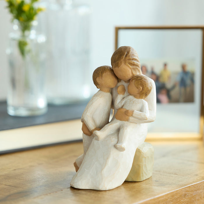 Wooden figurine of a mother and two children hugging on a wooden surface with a blurred background.