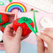 Strawberry-shaped product with green stem held by hands against a colorful background