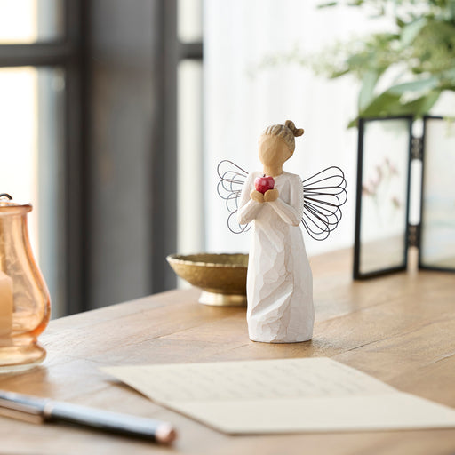 Standing angel in cream dress with wire wings, holding large, shiny red apple in outstretched hands