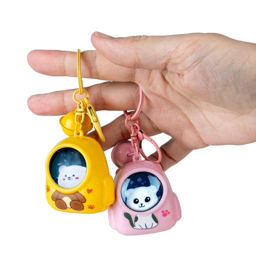 Hand holding two cartoon character keychains, one yellow and one pink, on a white background.
