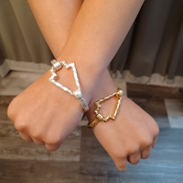 Two hands wearing gold and silver geometric bracelets on a neutral background