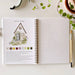 Open book with garden-themed illustration and color swatches on a white surface with greenery.