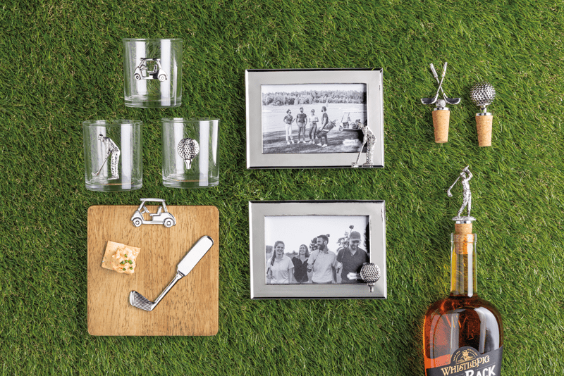 Collection of Whistleback brand items including glasses, frames, and bottle on a grassy background