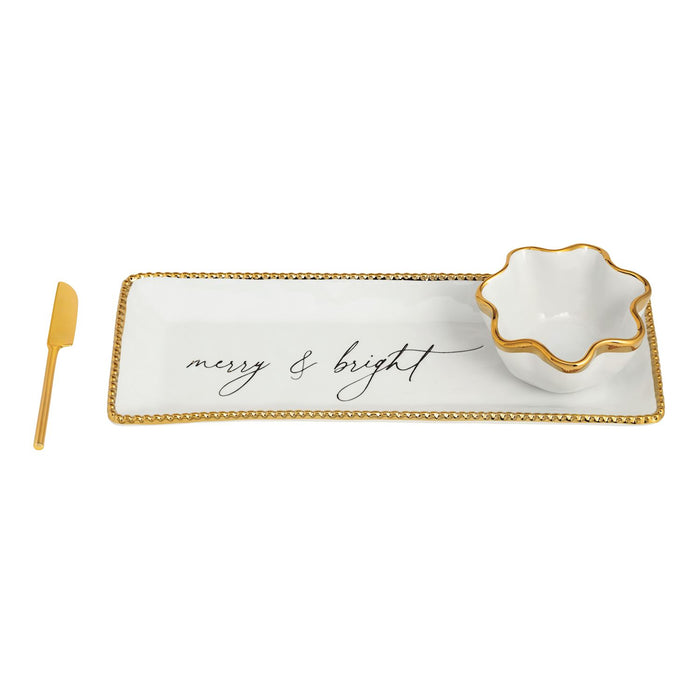 White tray with gold rim and 'merry & bright' text, accompanied by a white bowl and gold knife on a white background.